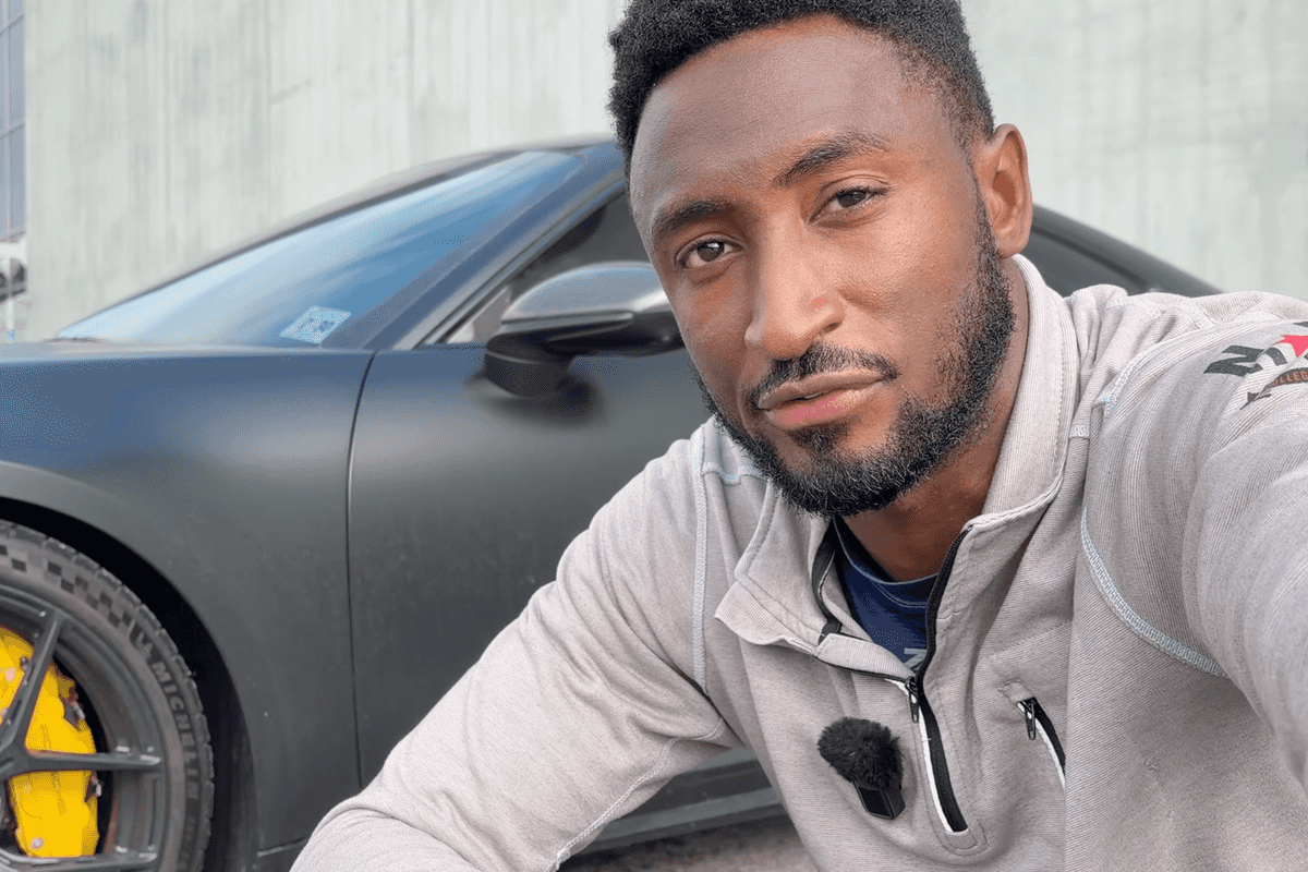 Marques Brownlee, a bearded Black man with short black hair, crouches in front of a black Tesla.