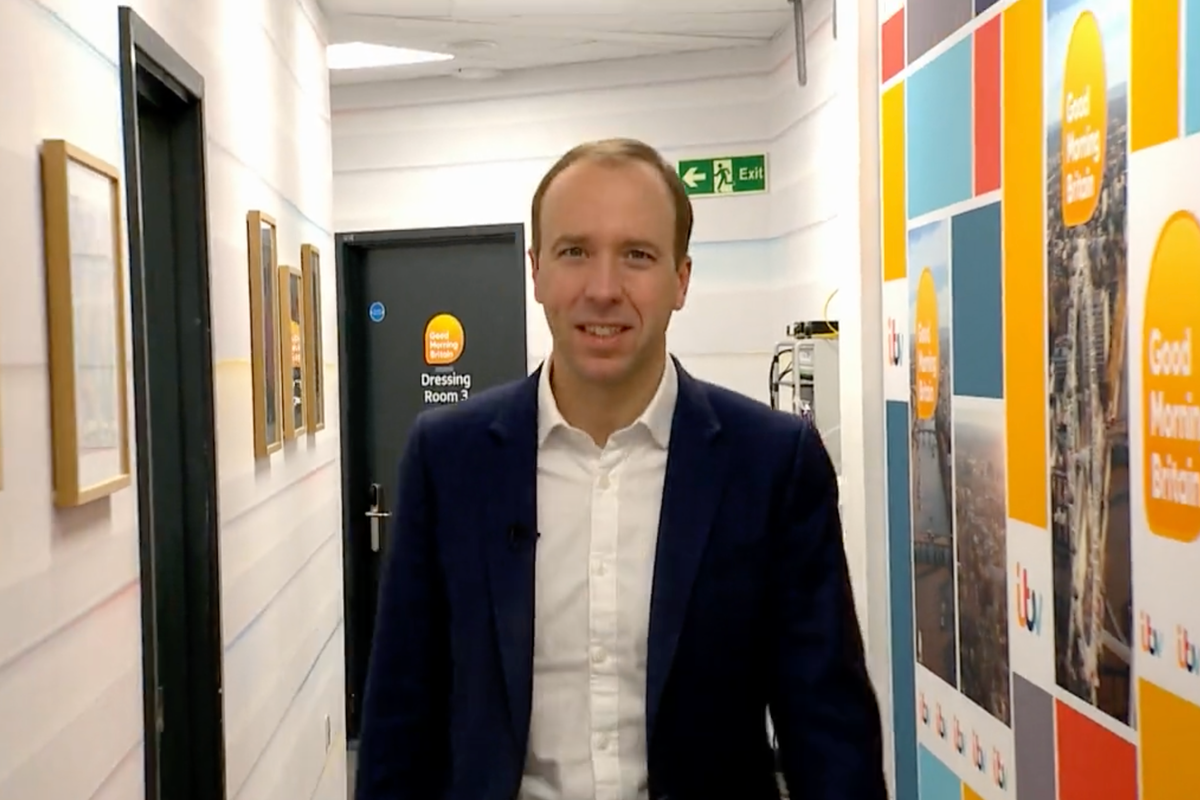 Matt Hancock, a white man with short brown hair, a large forehead and a blue suit, walks down a corridor in the Good Morning Britain studio. He's smiling awkwardly.