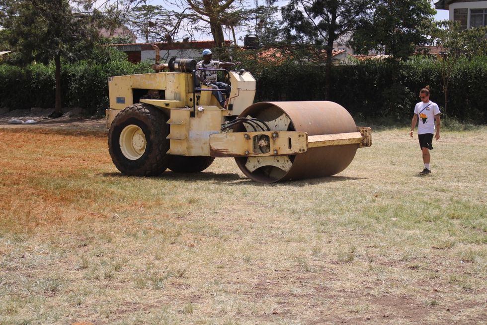 Max Keens standing next to a steamroller on a pitch in Kenya