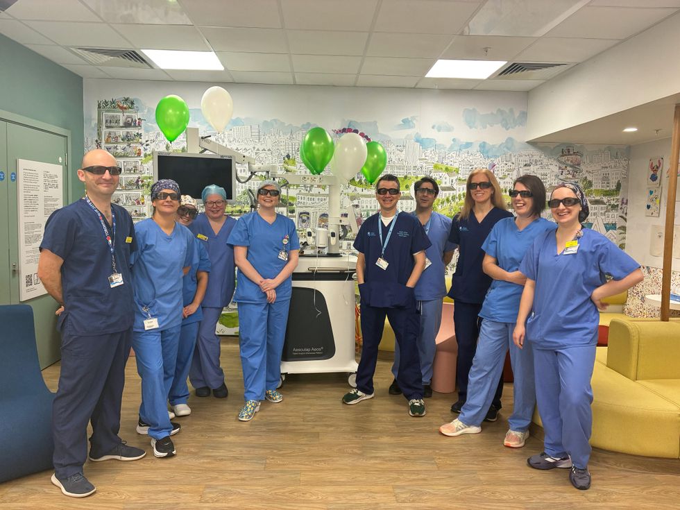 Medical staff, wearing dark glasses, smile while posing for a photo with the surgical device