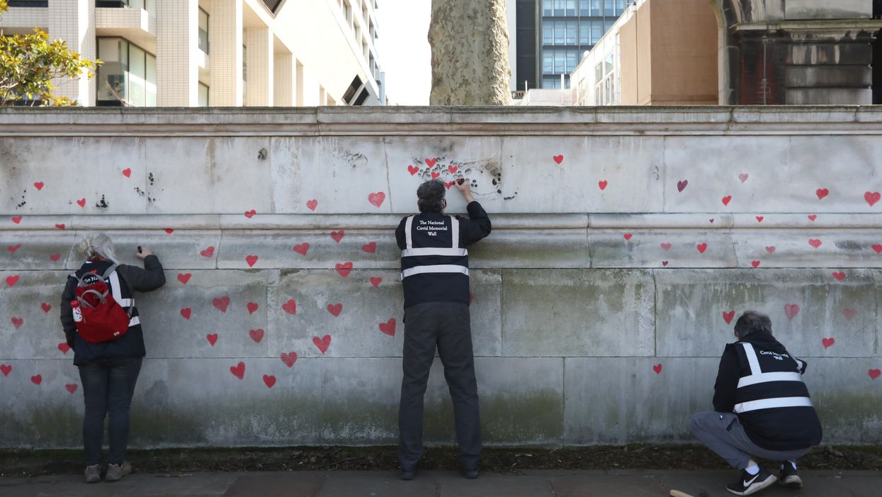 Members of bereaved families paint red hearts on the Covid-19 Memorial Wall