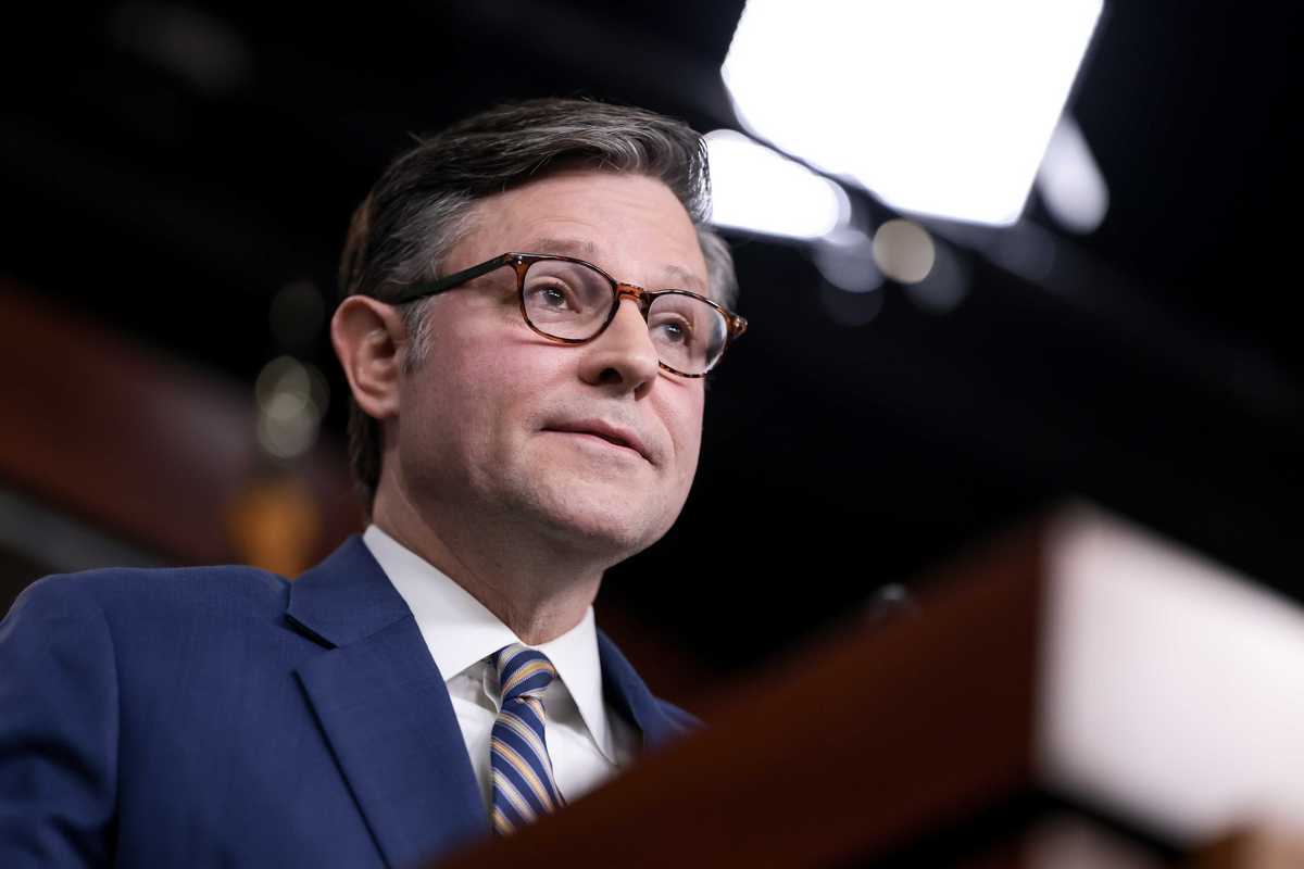 Mike Johnson, a white man with short black hair and glasses, speaking behind a wooden lectern.