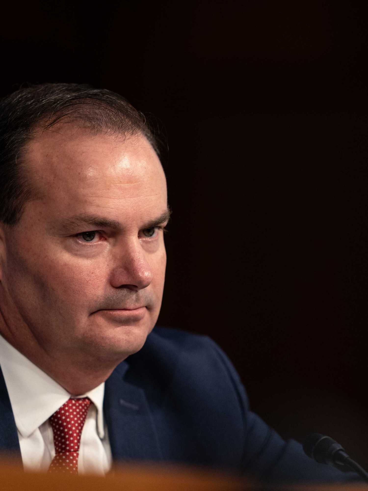 Mike Lee, a white ma n with short black hair and a blue suit, sitting at a congressional hearing.