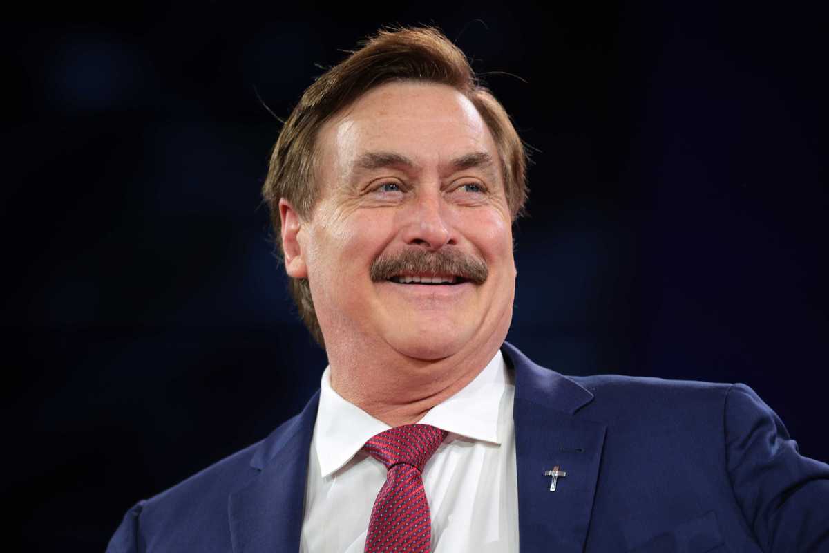 Mike Lindell, a white man with short brown hair, a blue suit and a moustache, smiling.