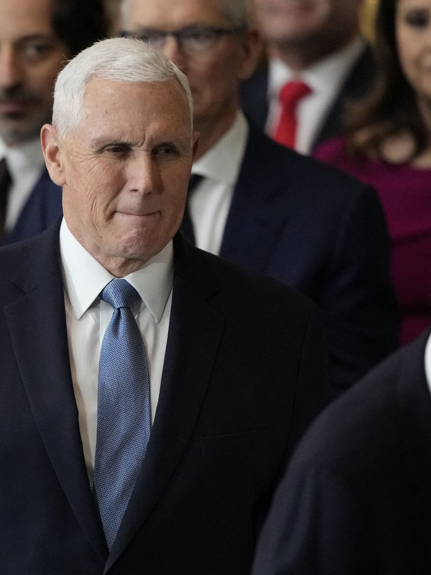 Mike Pence in a navy suit in amongst a huddle of people.