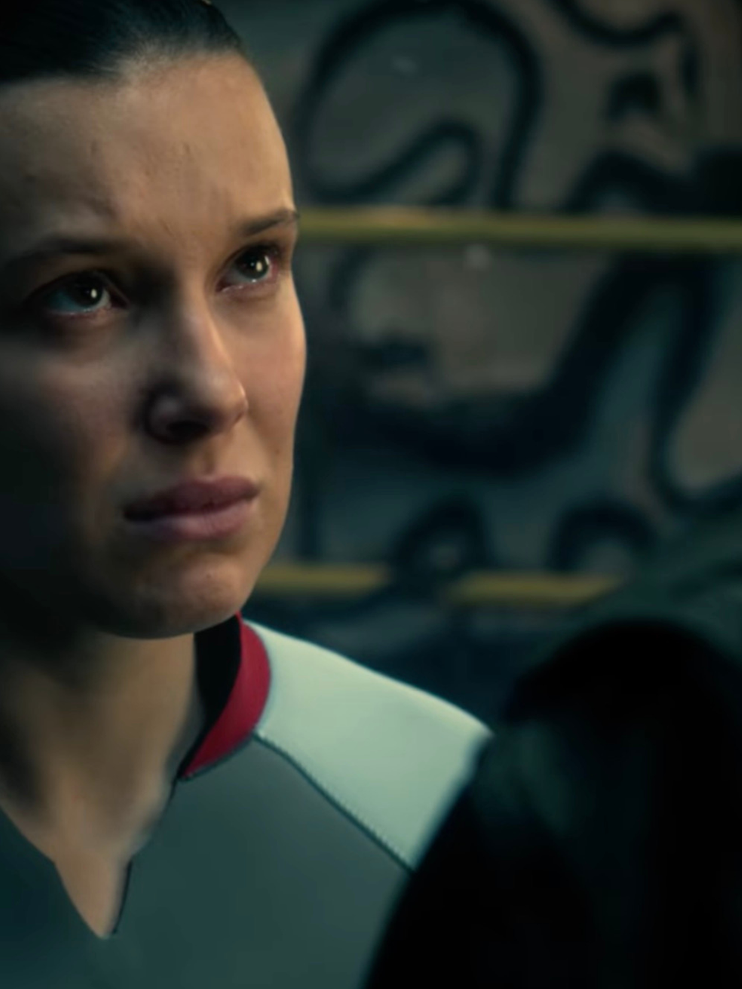 Millie Bobby Brown as Eleven in Stranger Things, wearing a grey swimsuit.