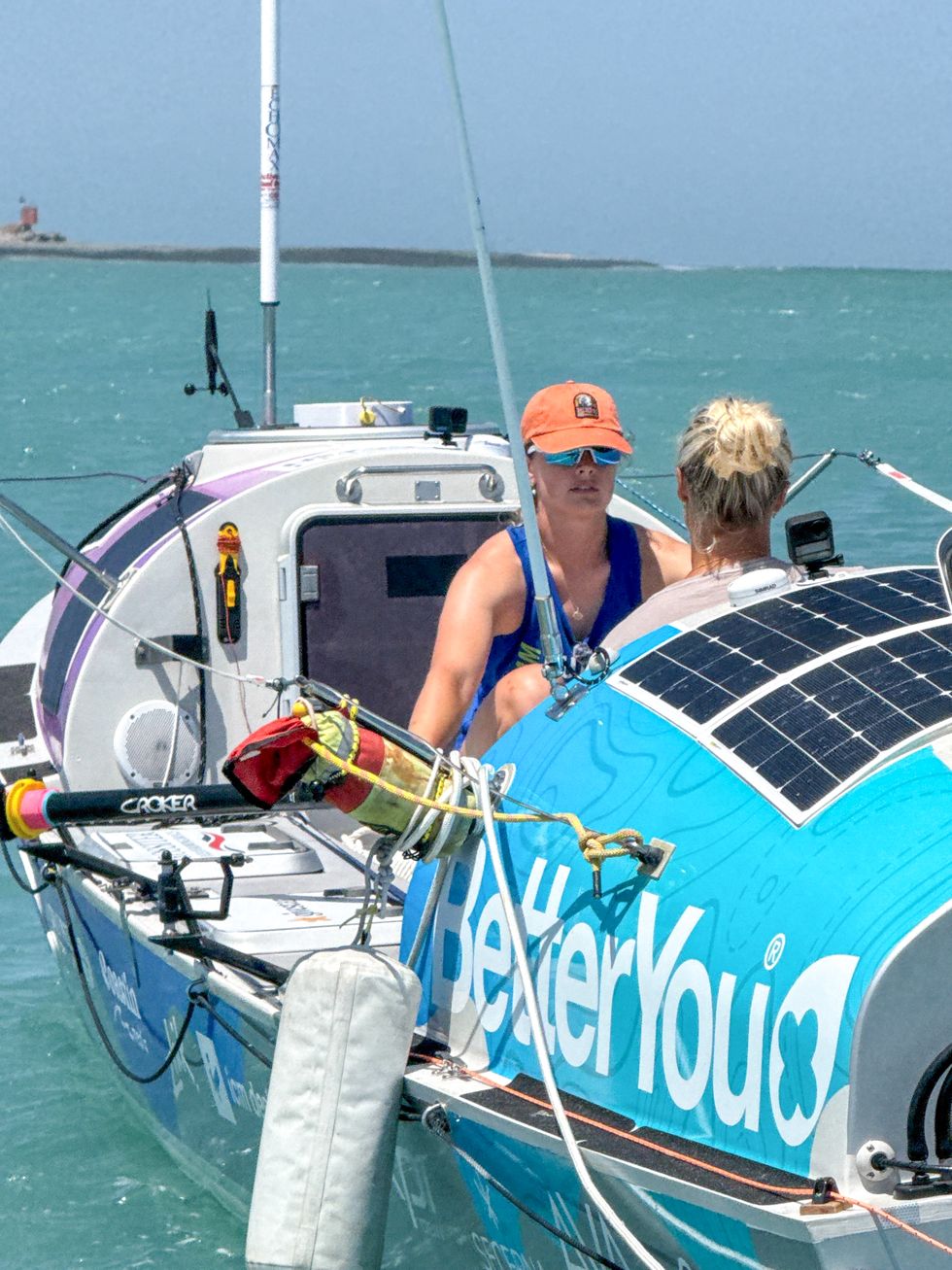 Miriam (left) and Jess (right) in a multicoloured boat on the sea with a pale blue sky in the background