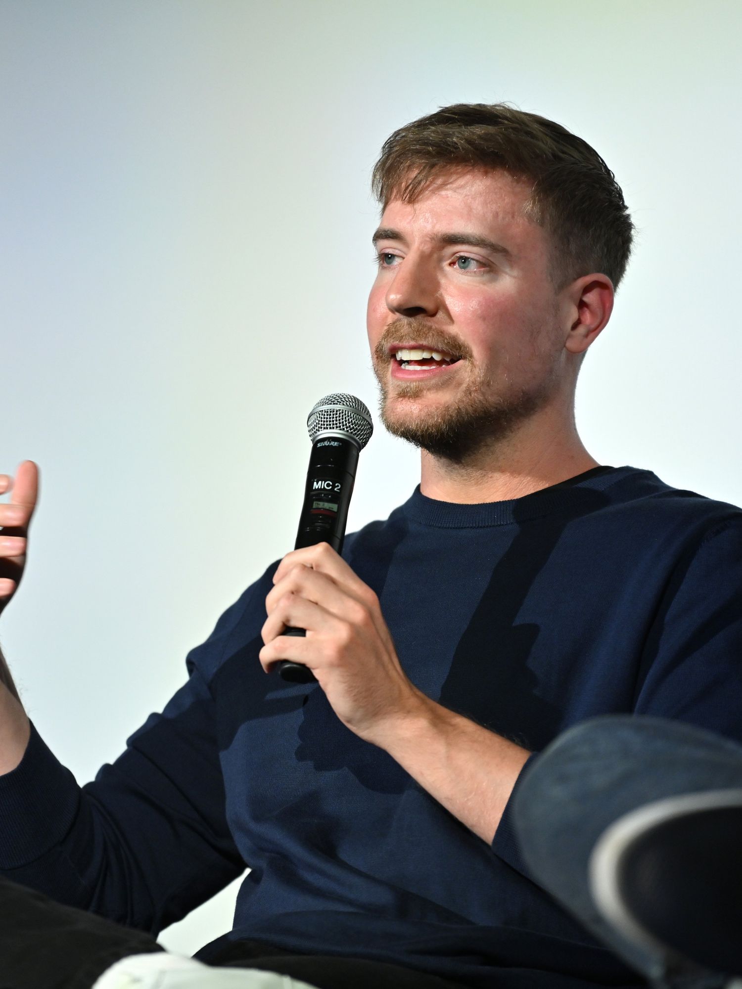 MrBeast, a bearded white man with short brown hair and a blue jumper, sits and speaks into a microphone at a screening.