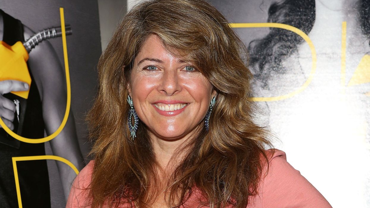 Naomi Wolf, a white woman with shoulder length bushy brown hair and a pink shirt, smiles at the camera.