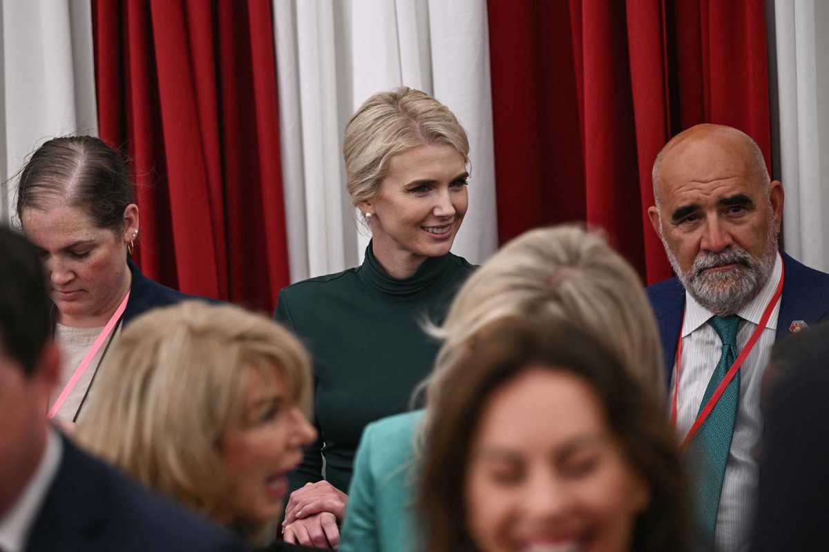Natalie Harp, a white woman with short blonde hair, looking to her left and smiling at something off-camera, in a room full of people.