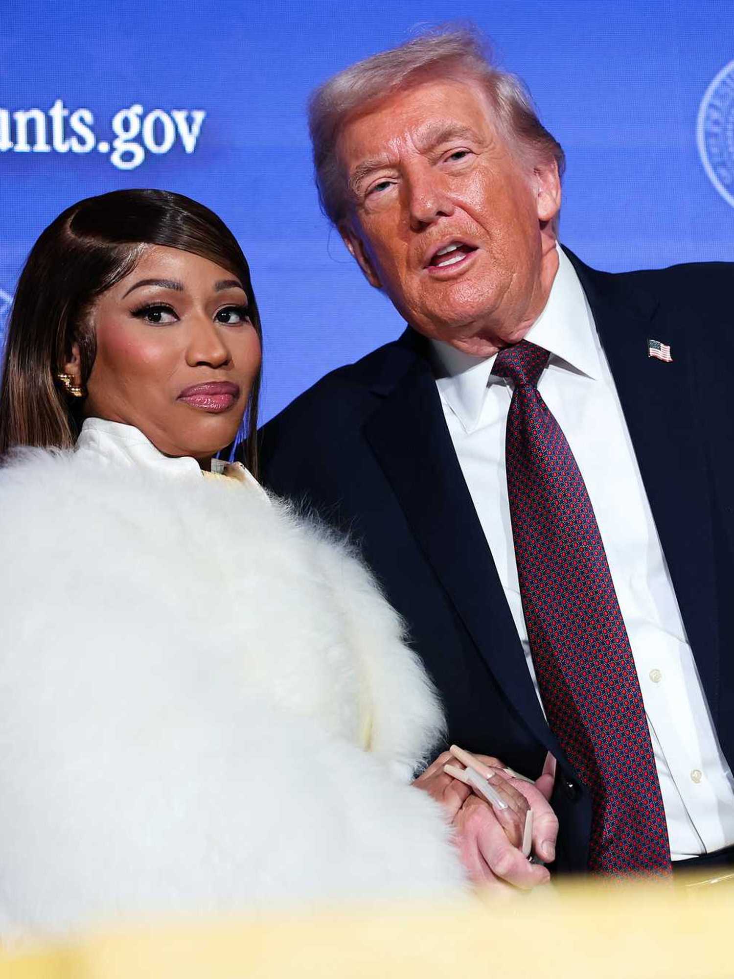 Nicki Minaj in a white fur jacket standing next to Donald Trump in a black suit with a purple tie.