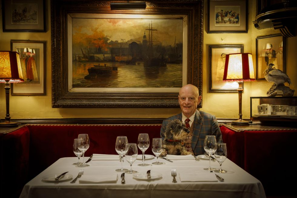Owner J-P Mayhew sits at a formally-laid dining table with his dog, and a painting behind them