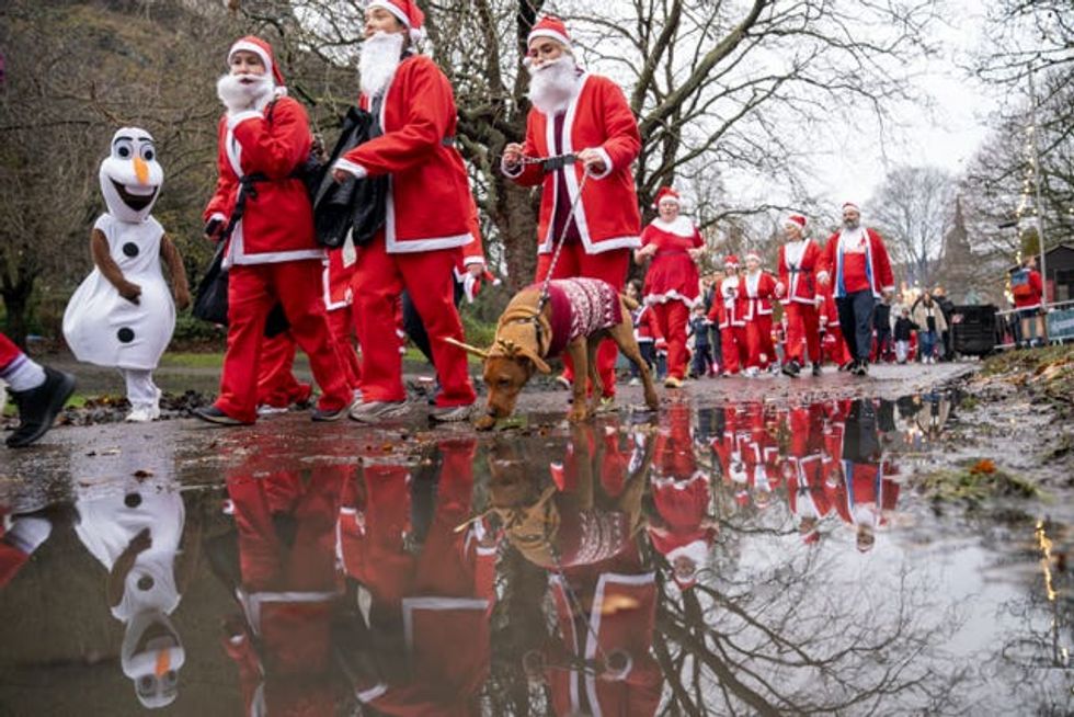 People dressed as Santa walk past a puddle with a dog