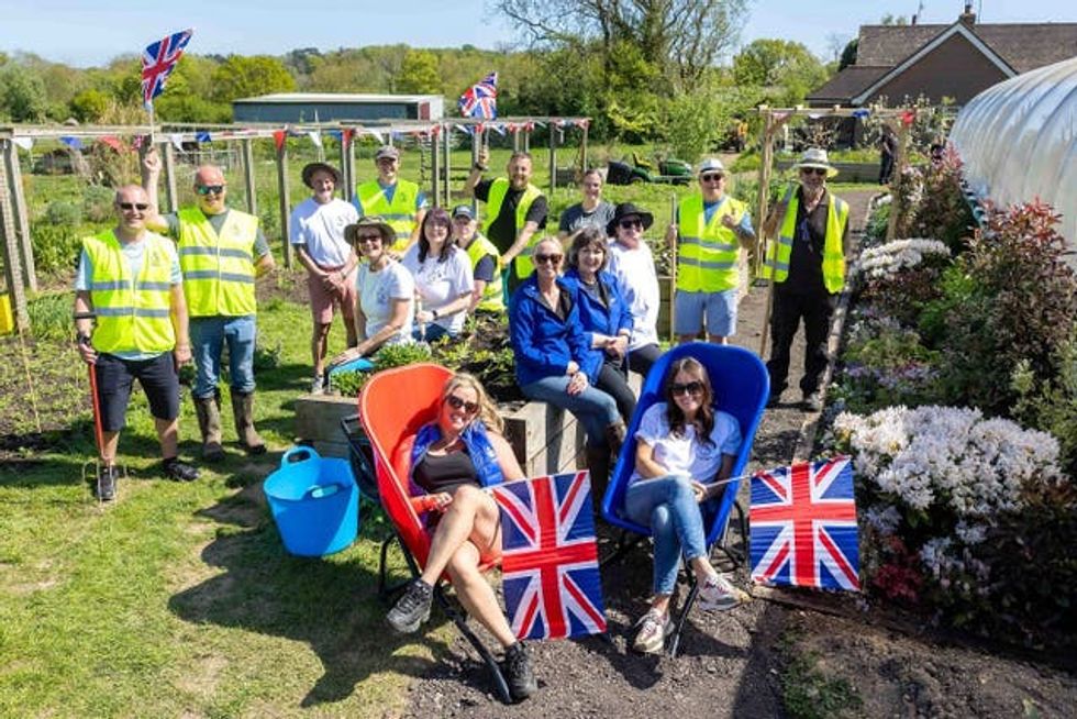 People, some wearing hi-vis, some holding spades and some waving Union flags, raise their hands in the air at a garden created at the Veterans' Growth centre near Battle, East Sussex