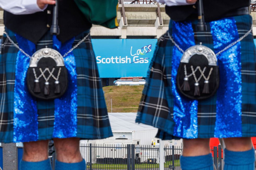 People standing in front of the sign, amended to say Scottish Lass, while wearing kilts