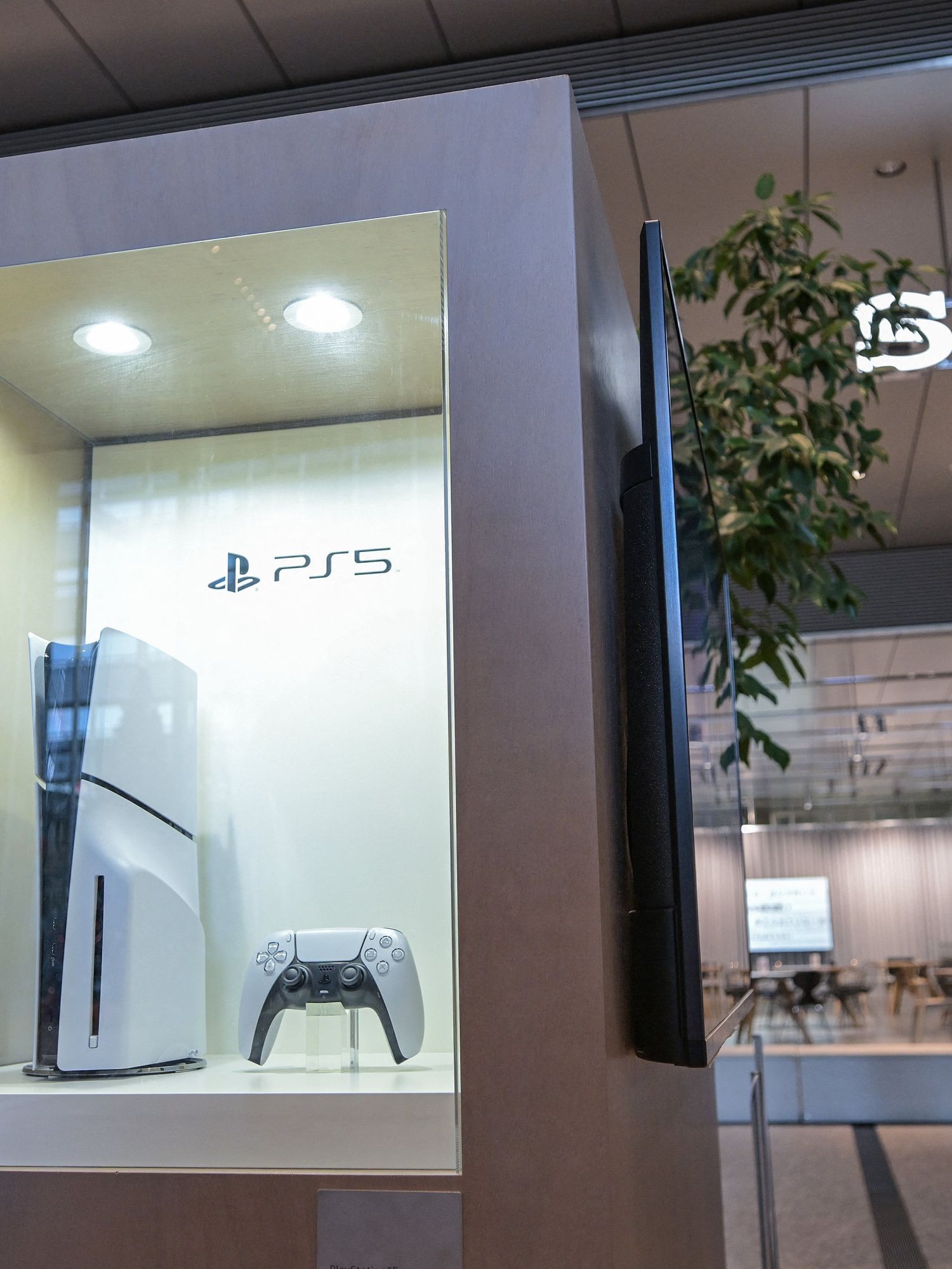 People walk past a display case (L) showing a new PlayStation 5, in the lobby of the Sony headquarters building in central Tokyo on November 27, 2024