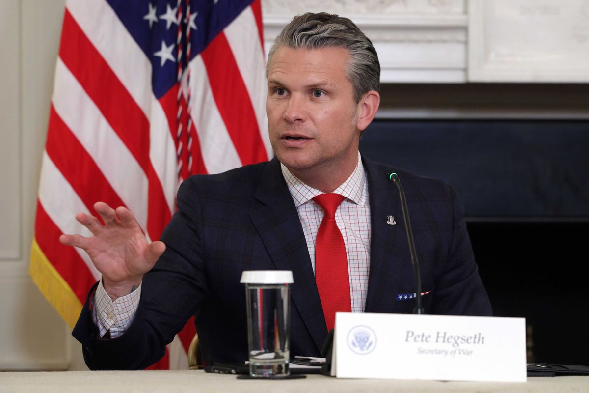 Pete Hegseth, a white man with short grey hair, a black suit and a red tie, talking from beind a desk.