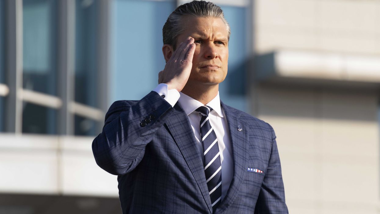 Pete Hegseth in a blue suit and tie, saluting.