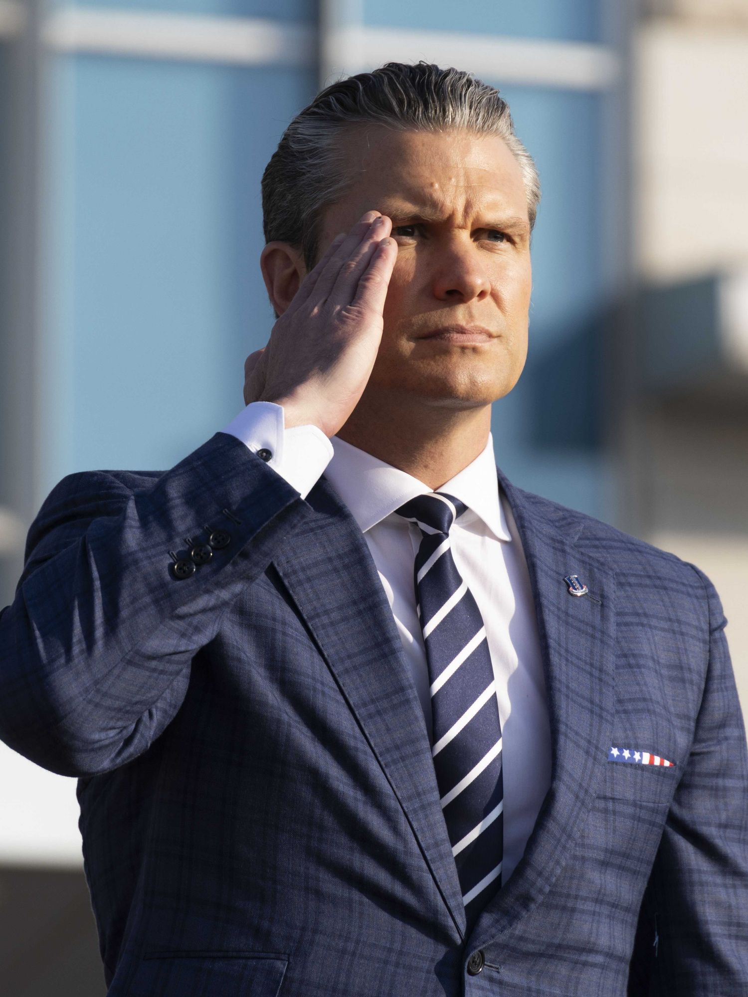 Pete Hegseth in a blue suit and tie, saluting.