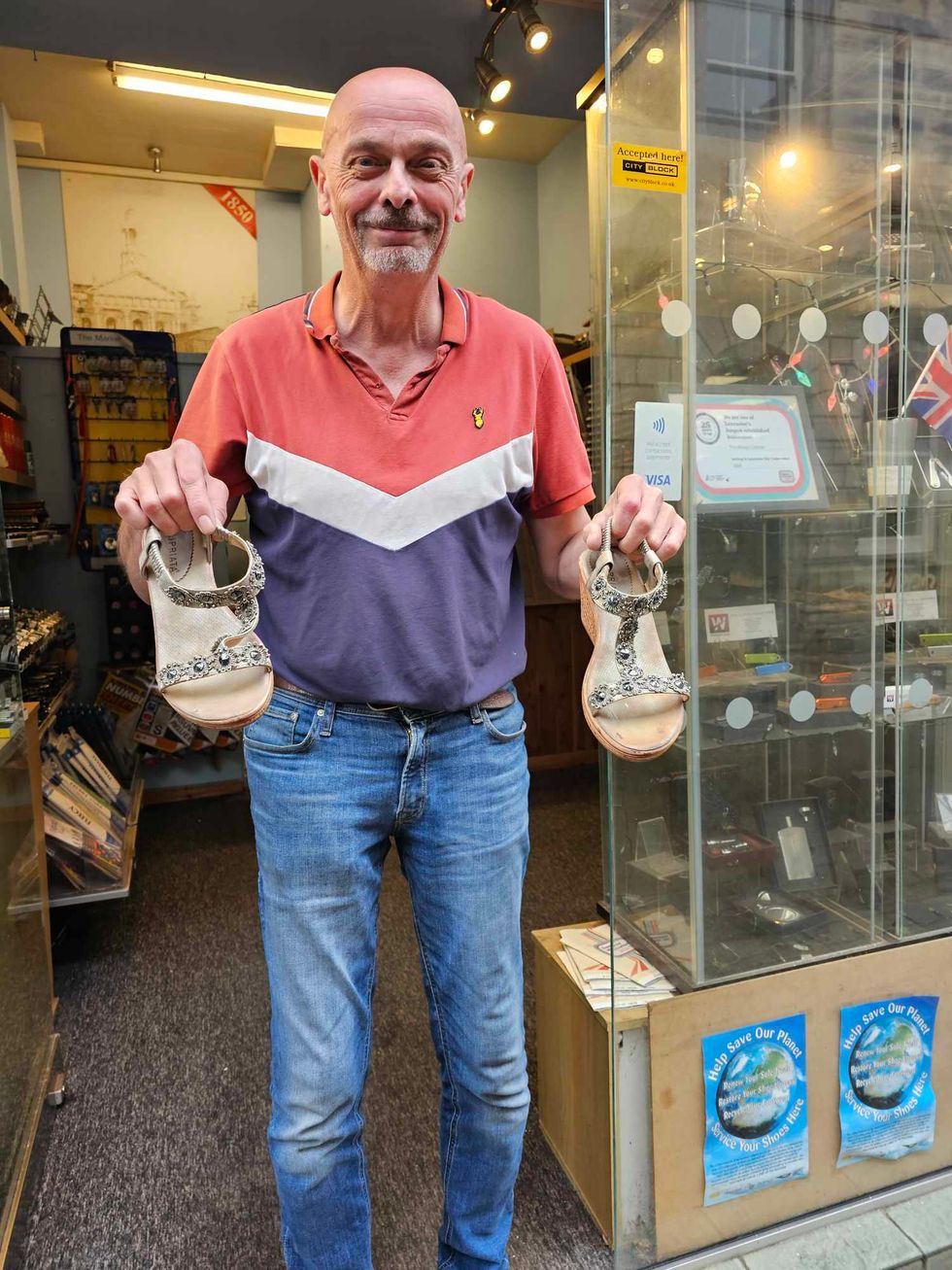 Peter Corke smiling as he holds up the shoes outside of his shop