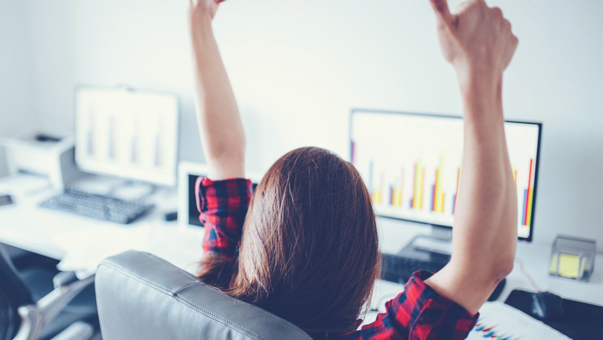 Portrait of happy young successful businesswoman celebrate something with arms up. Happy woman sit at office and look at Computer/ laptop. Positive emotion.