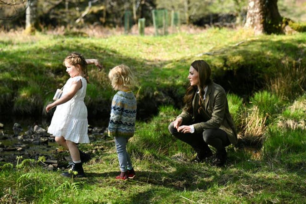 Princess of Wales crouching down beside two young girls throwing sticks
