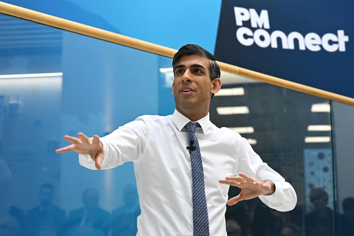 Rishi Sunak, a brown man in a white shirt and blue tie, has his hands splayed out in front of him while speaking. It looks like he's doing a terrible surfing impression.