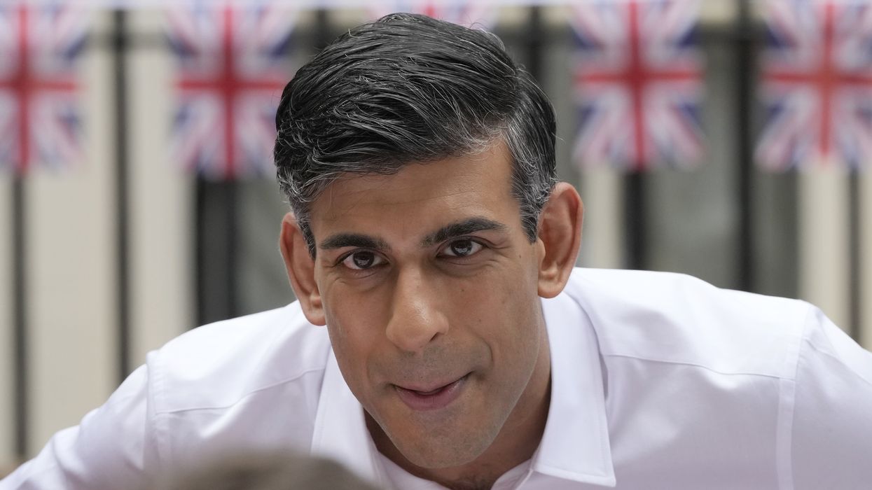 Rishi Sunak in a white shirt talking to a guest outside Downing Street. Union Jack bunting can be seen behind him draped along the black metal gates of No 10.