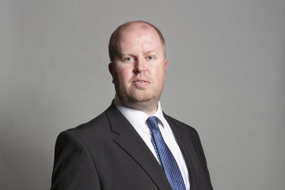 Rob Roberts, a white man with a stubbly brown beard and short brown hair. He has a large forehead and wears a black suit.