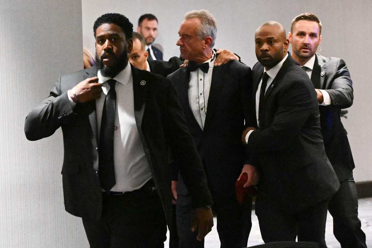 Robert F Kennedy Jr is escorted from the White House Correspondents' Dinner by federal agents in suits.