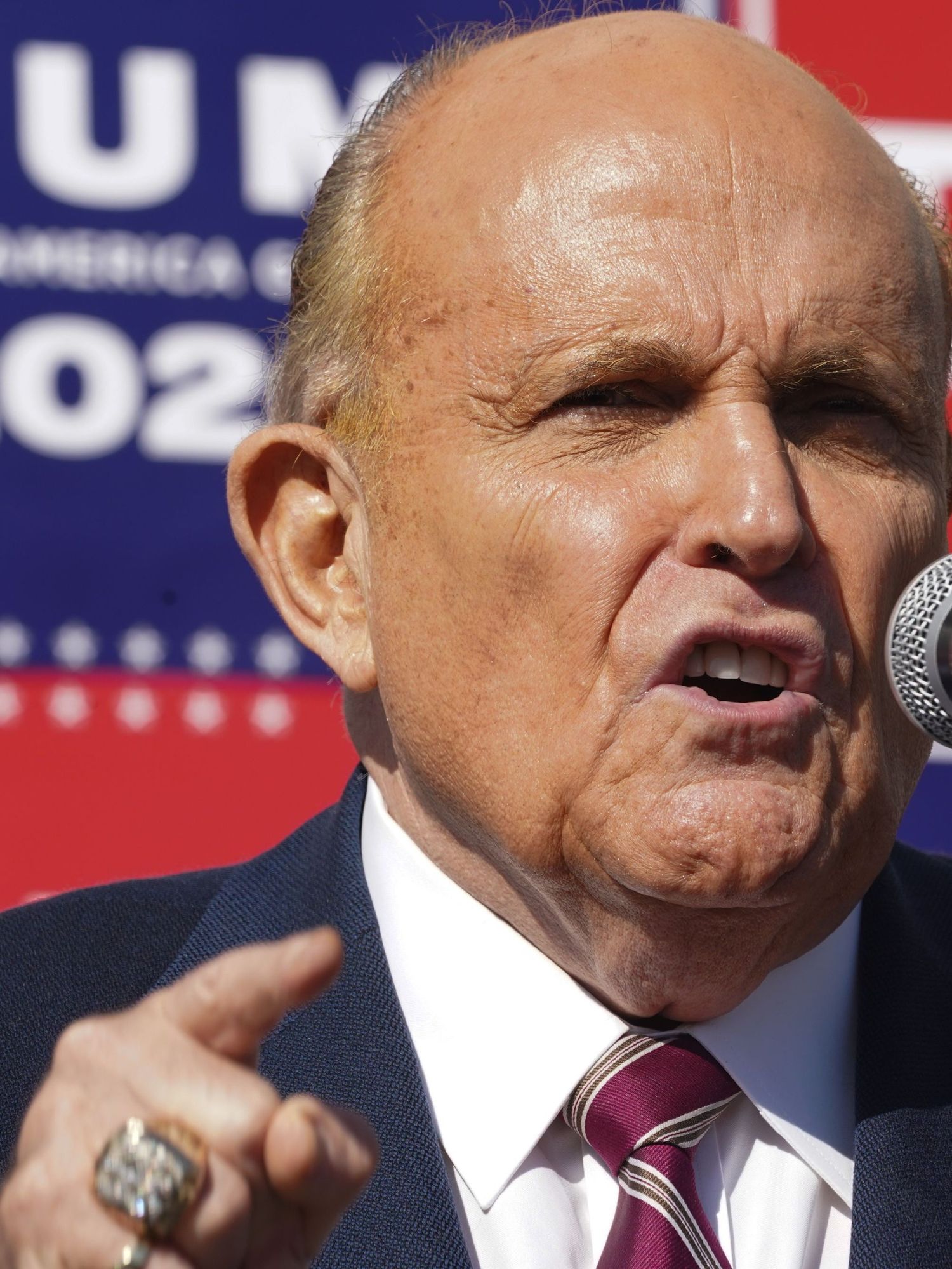 Rudy Giuliani, a white man with a large forehead, short blonde hair and a blue suit, speaks into a microphone at a Trump press conference.