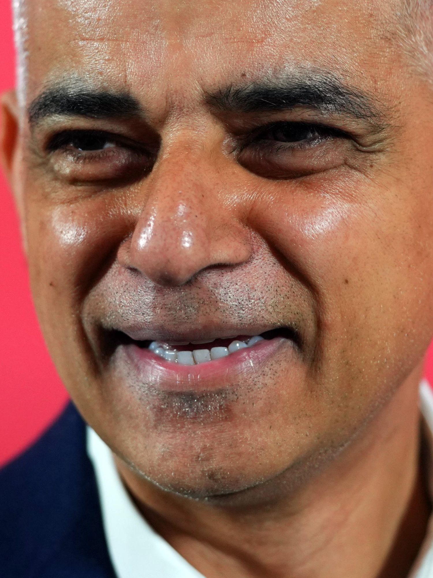 Sadiq Khan, smiling against a red background.