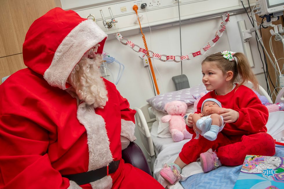 Santa speaking to a little girl who is holding a baby doll