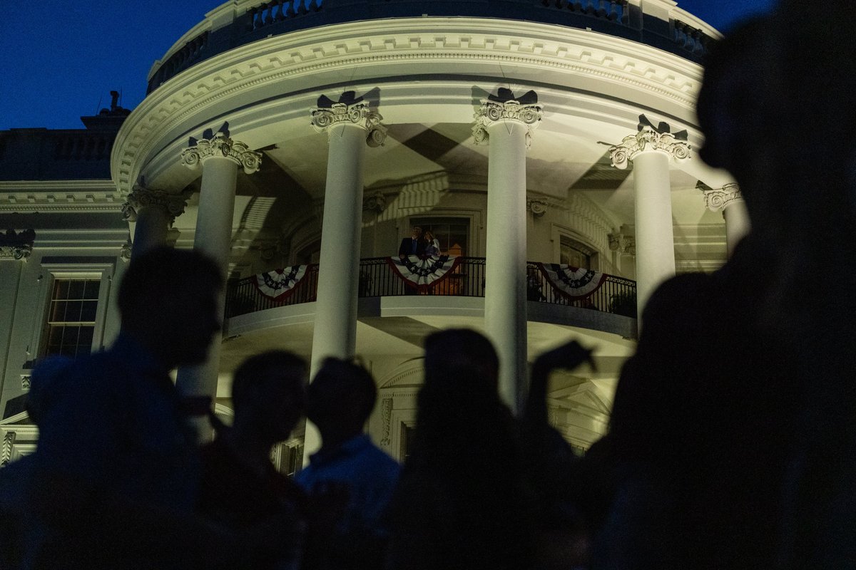 Silhouetted figures gather outside the White House at night.