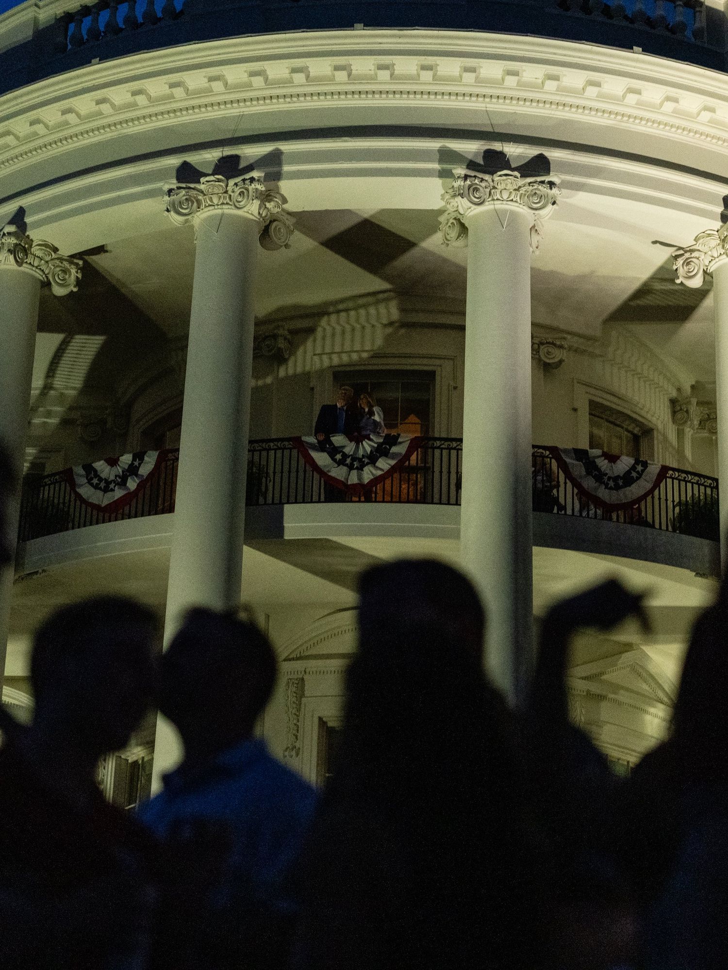 Silhouetted figures gather outside the White House at night.