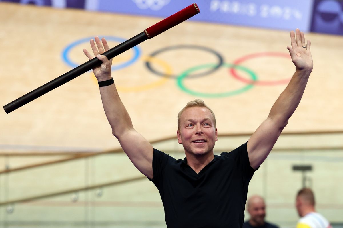 Sir Chris Hoy in the velodrome at the Paris 2024 Olympic Games, raising both hands in the air and holding a black pole in his right.