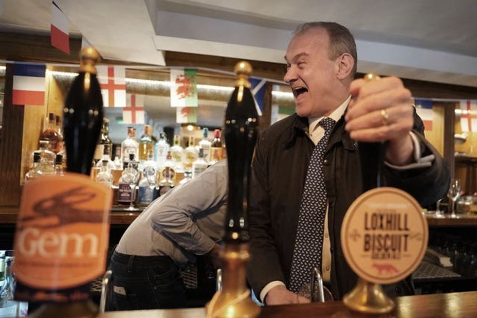 Sir Ed Davey, wearing a dark jacket, pulls a pint behind a bar