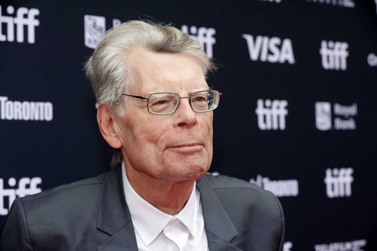 Stephen King smiling in front of black posterboard.