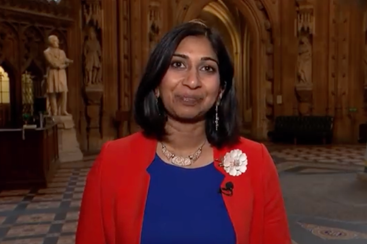 Suella Braverman, a brown woman with short black hair, a red fleece and blue dress, smiles as she stands in central lobby in the Houses of Parliament.