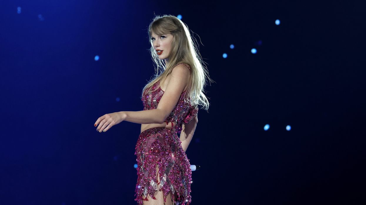Taylor Swift, a white woman with long blonde hair in a glittery pink dress, stands on stage during her Eras tour.
