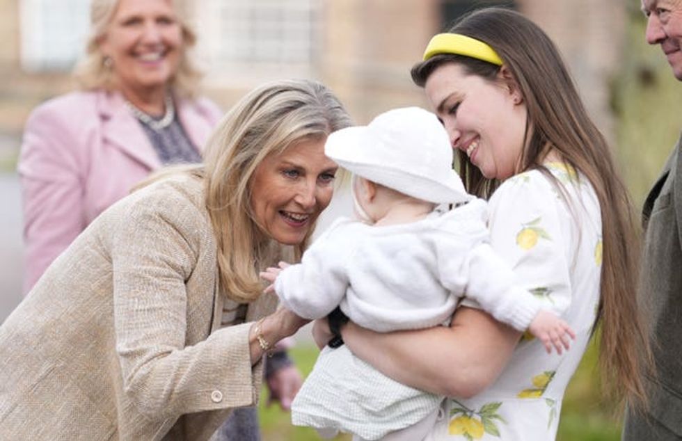 The Duchess of Edinburgh bends down as she plays with a baby being held by a young woman