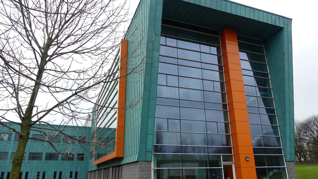 The front of a turquoise university building with rows of rectangular windows from top to bottom.