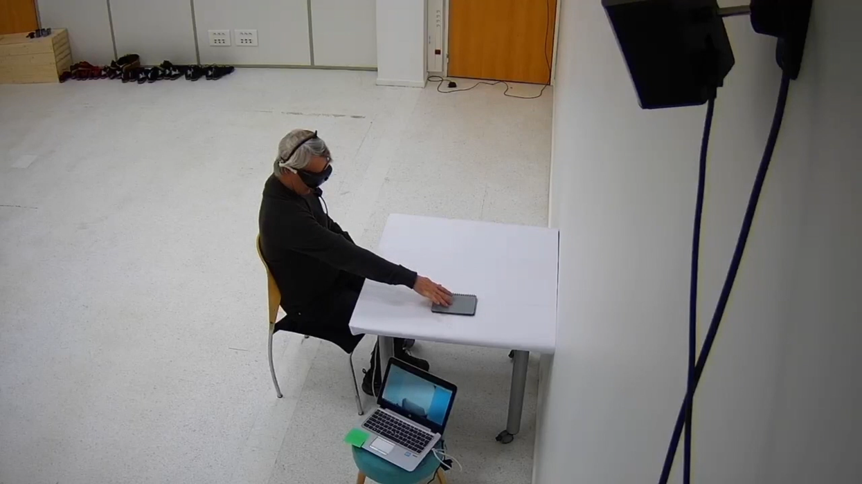 The patient doing a test of perceiving, locating, touching, and counting various objects placed on a white table while wearing light-stimulating goggles