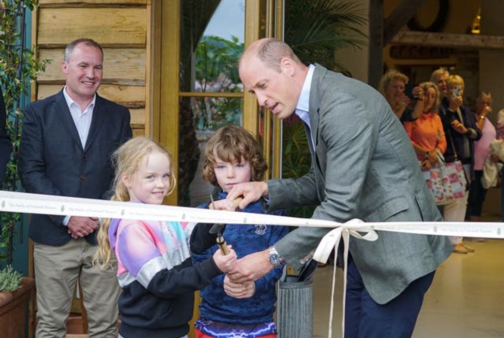 The Prince of Wales helps brother and sister James and Violet Scott to cut the ribbon during a visit to the Duchy of Cornwall nursery, near Lostwithiel, Cornwall