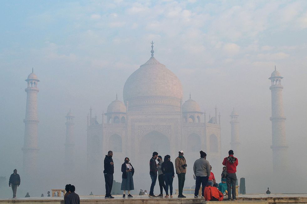 The Taj Mahal, a huge marble palace partially obscured by smog, with tourists in the foreground