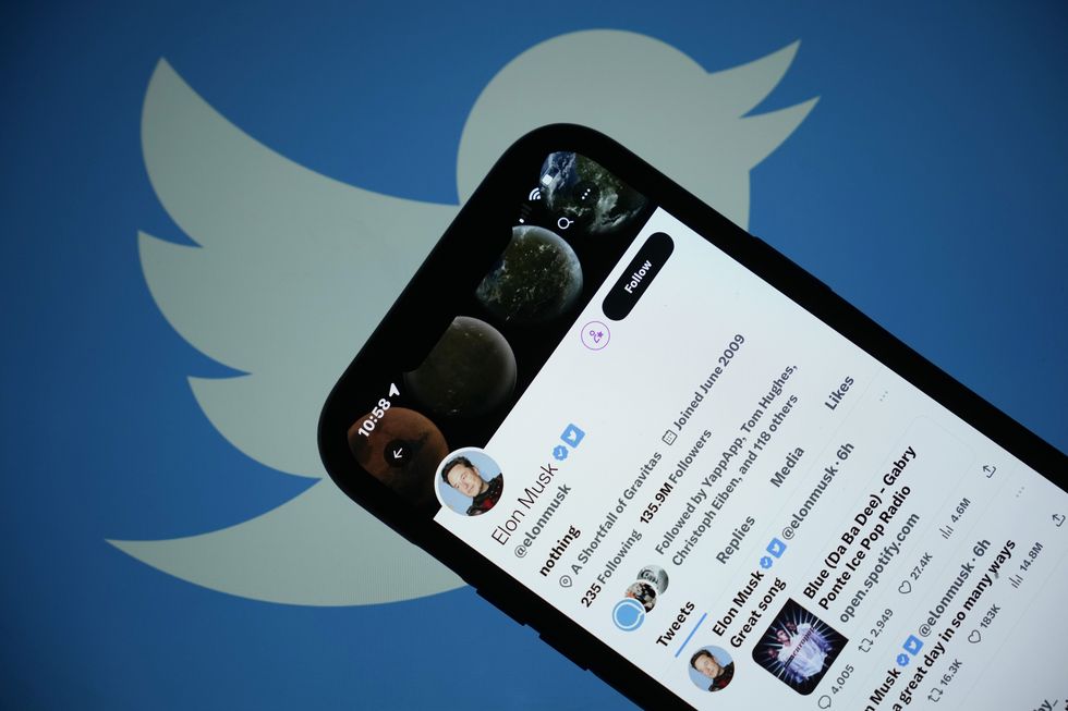 The Twitter account of Elon Musk is seen on a iPhone, with the white Twitter bird logo against a blue background visible behind it.