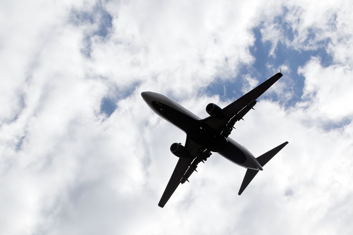 The underside of a passenger aeroplane flies overhead with clouds behind it.