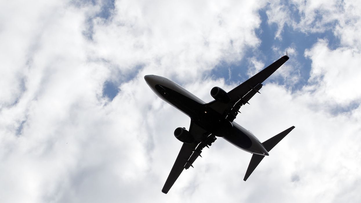 The underside of a passenger aeroplane flies overhead with clouds behind it.