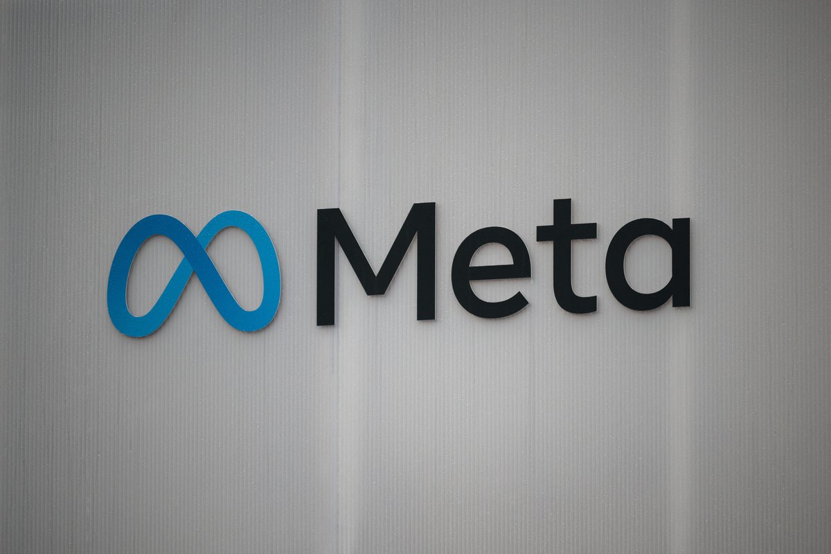 The word Meta and its blue infinity logo as a sign on a white wall.