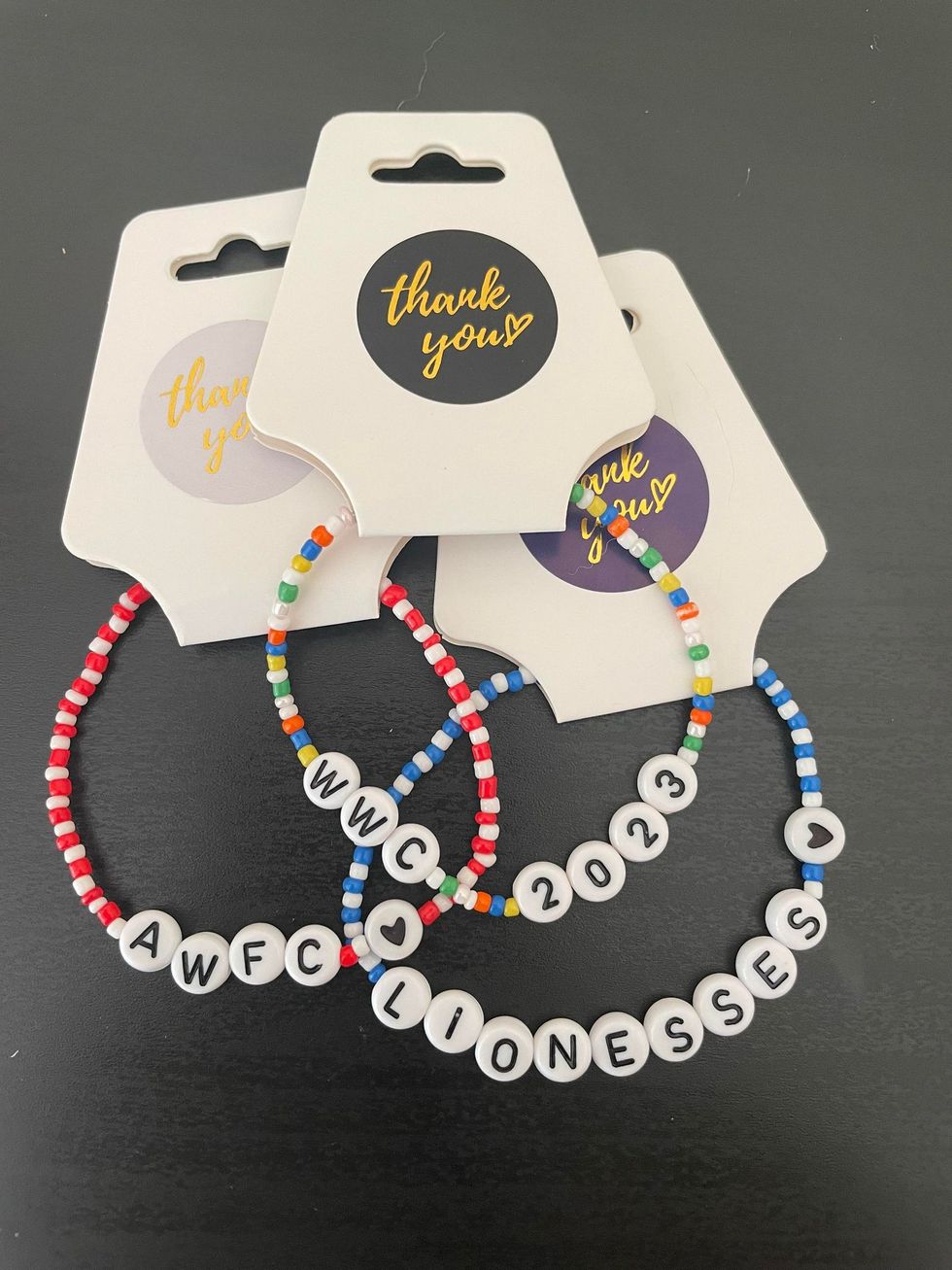Three of Caitlin's bracelets with beads spelling 'WWC 2023', 'Lionesses' and 'AWFC'